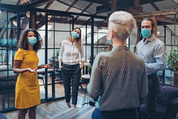 Group of team members wearing masks and standing at a distance in the office